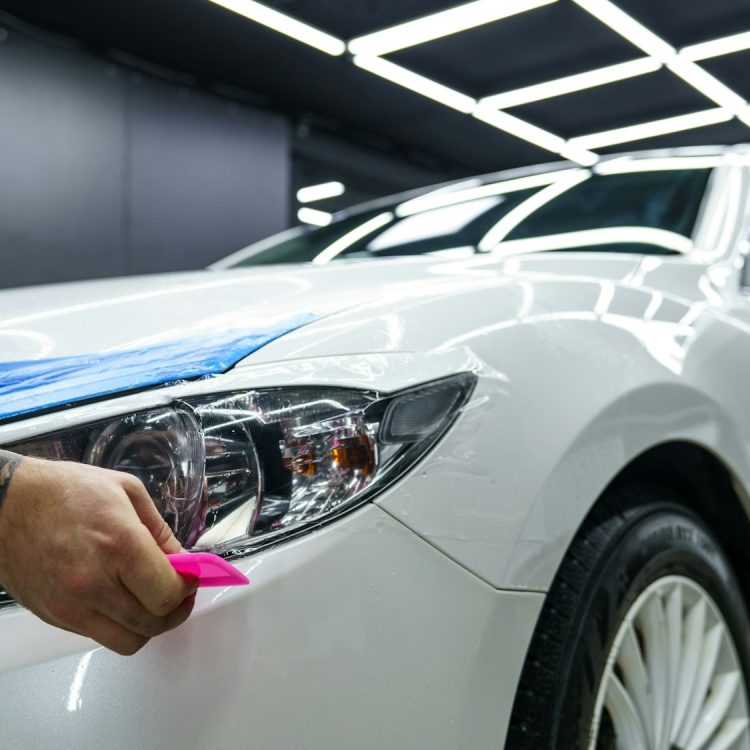 Sticker of a protective film on the headlight of a car in a car detailing studio